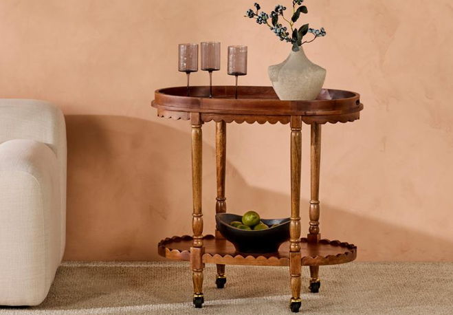 Wooden table with decorative vase and glasses against a peach wall.