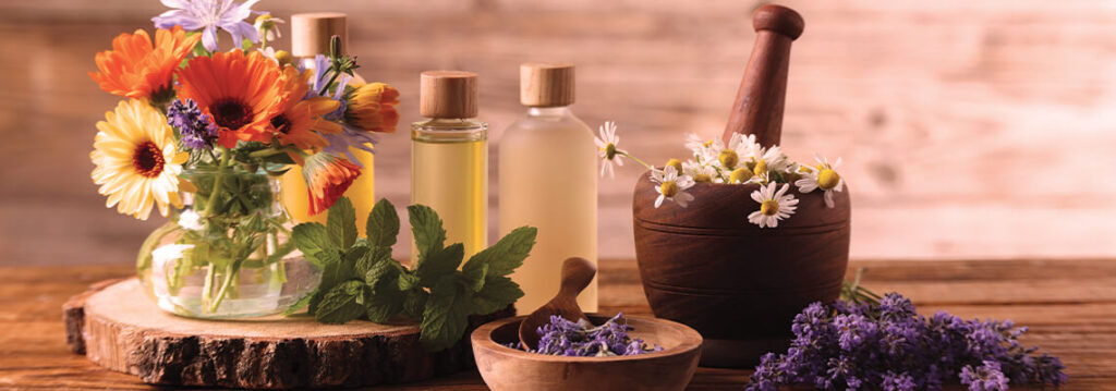 Bottles of essential oils, flowers, and herbs on a wooden surface.
