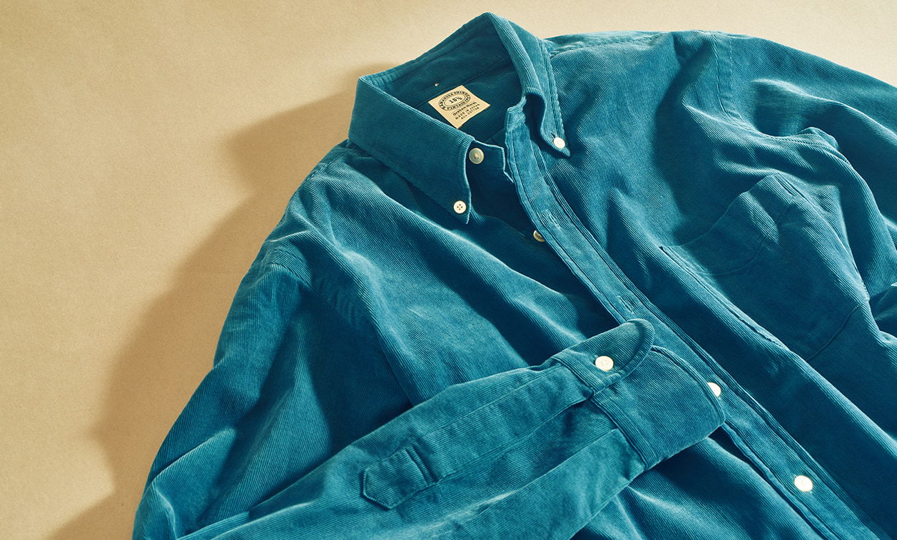A teal button-up shirt laid on a beige surface.