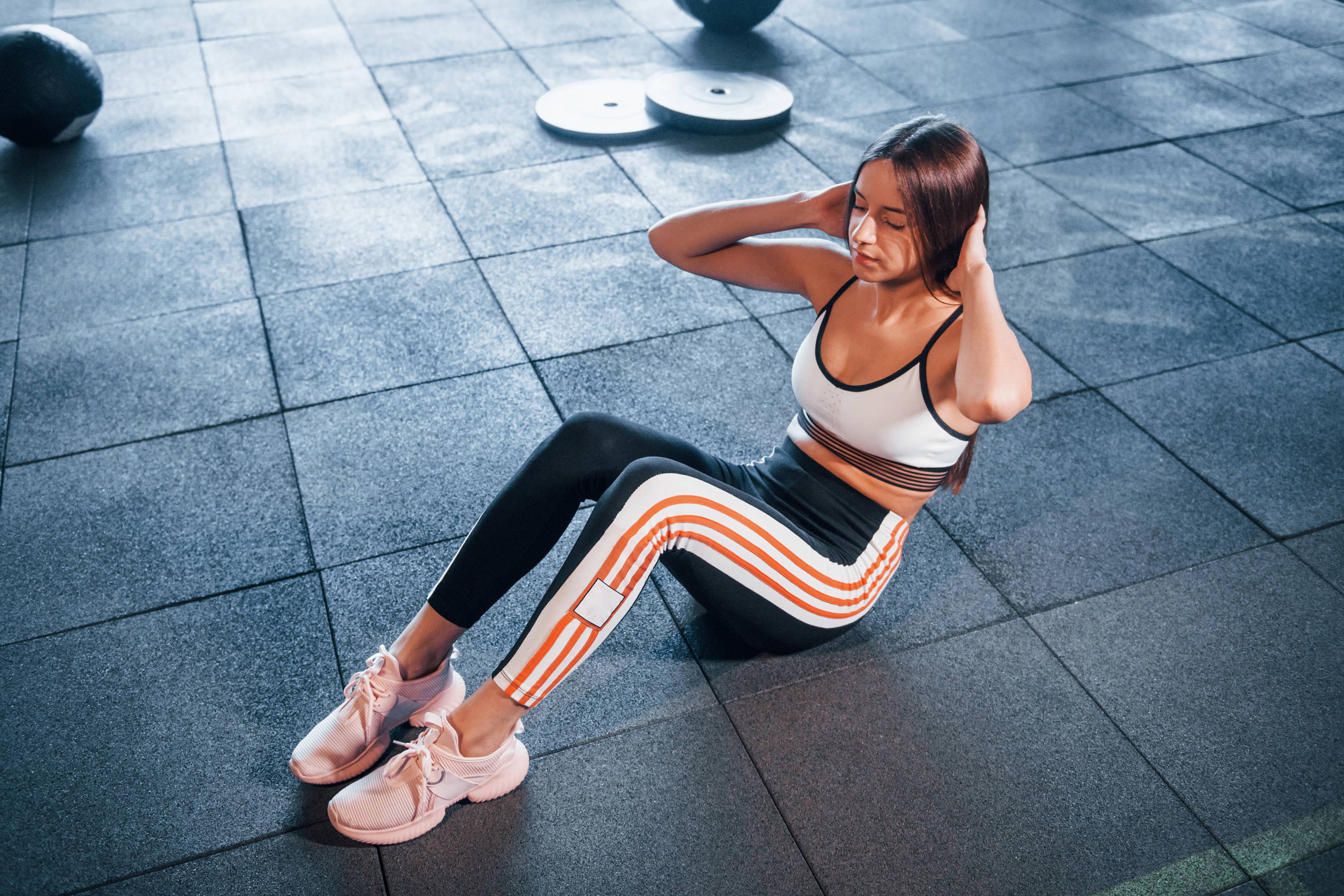 A girl doing a sit-up while sitting on black rubber gym flooring tiles.