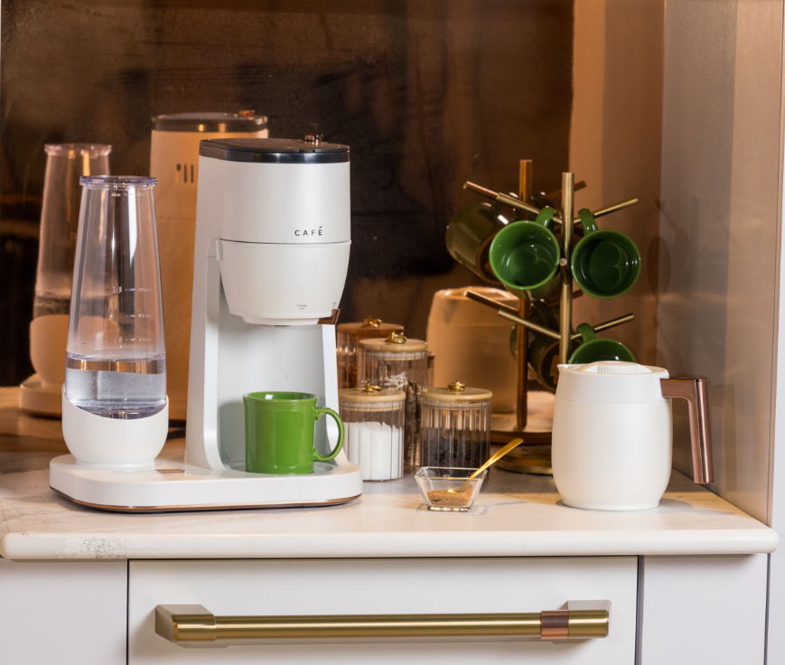 Coffee maker with cups, water container, and milk pitcher on a countertop.