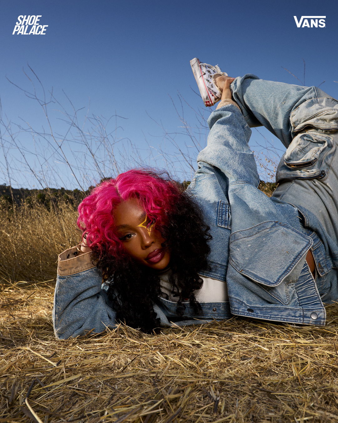 Person with pink hair in denim outfit lying on grass outdoors.