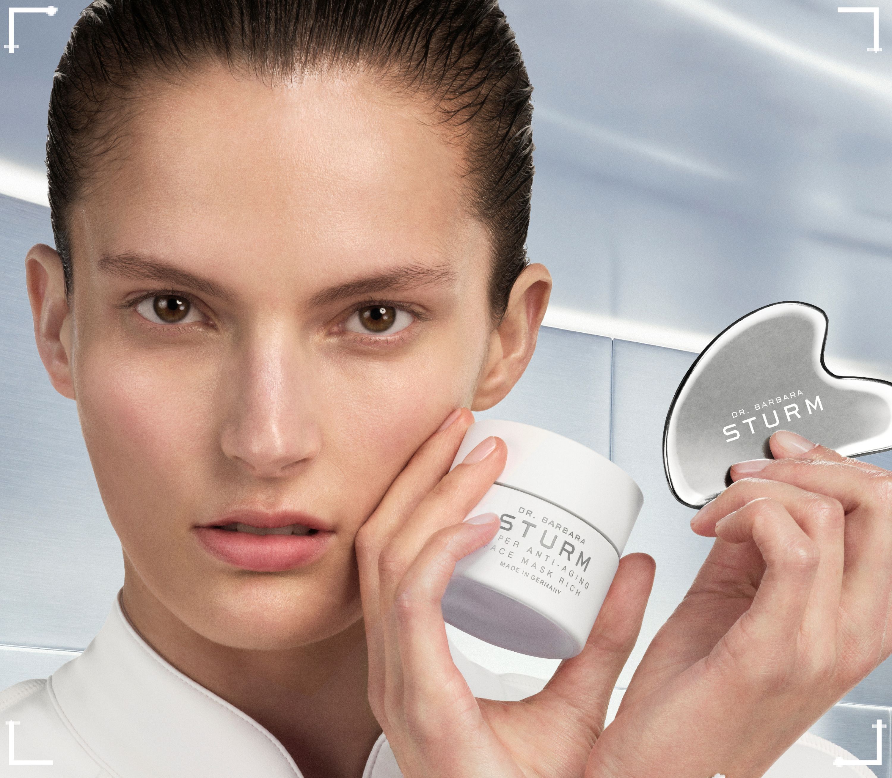 Model holding a skincare jar and a facial tool, looking at the camera.