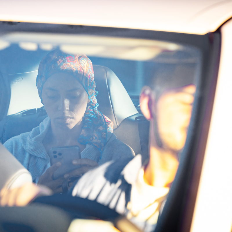 A woman using her phone in a car with a driver.