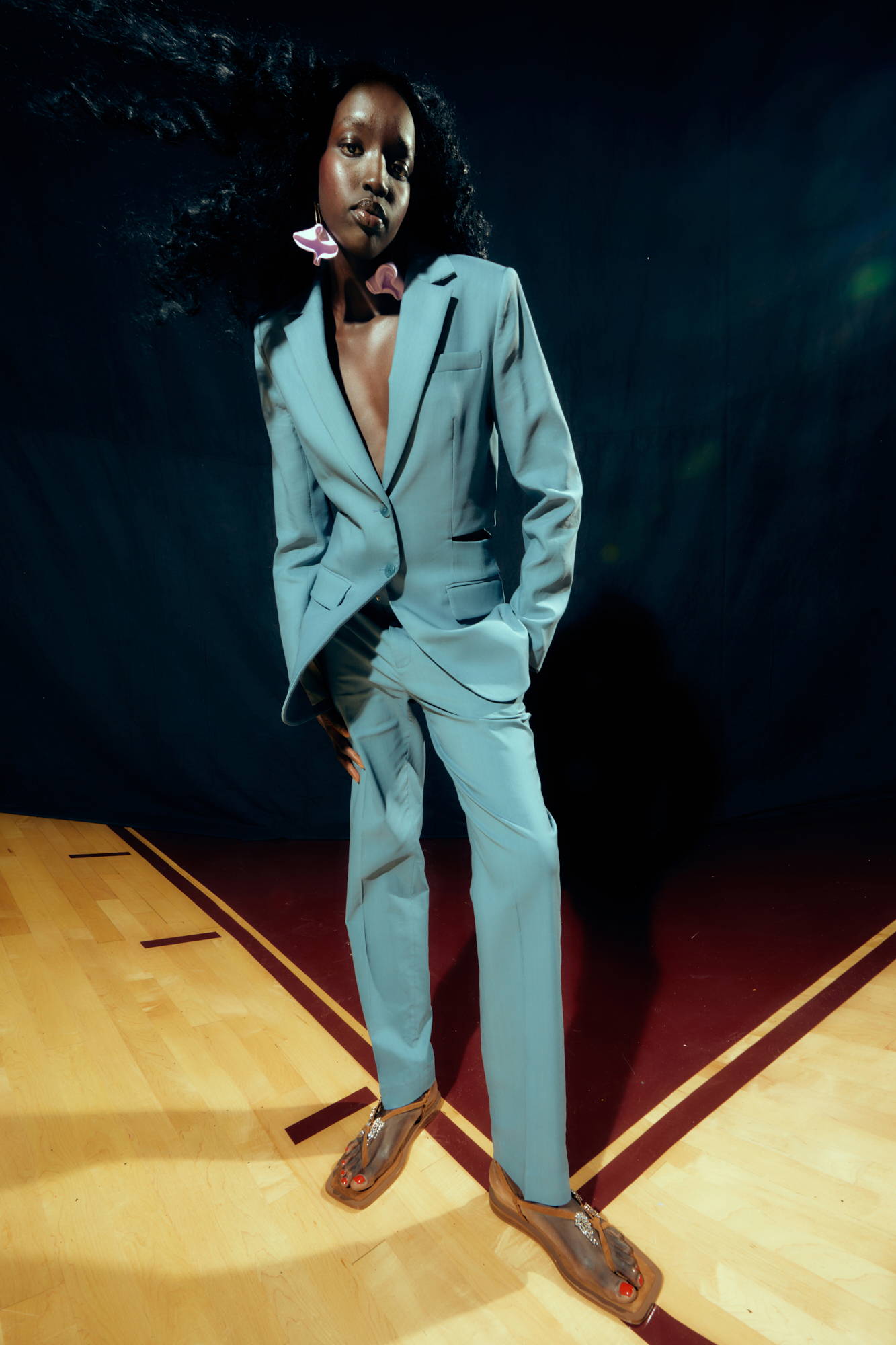 Person in a gray suit poses confidently on a wooden floor.