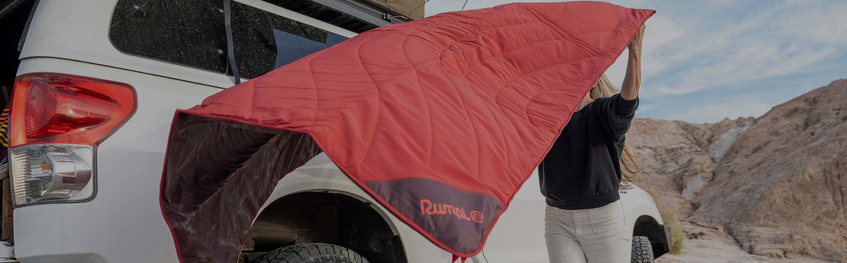 Person setting up a red awning by a vehicle in a desert landscape.