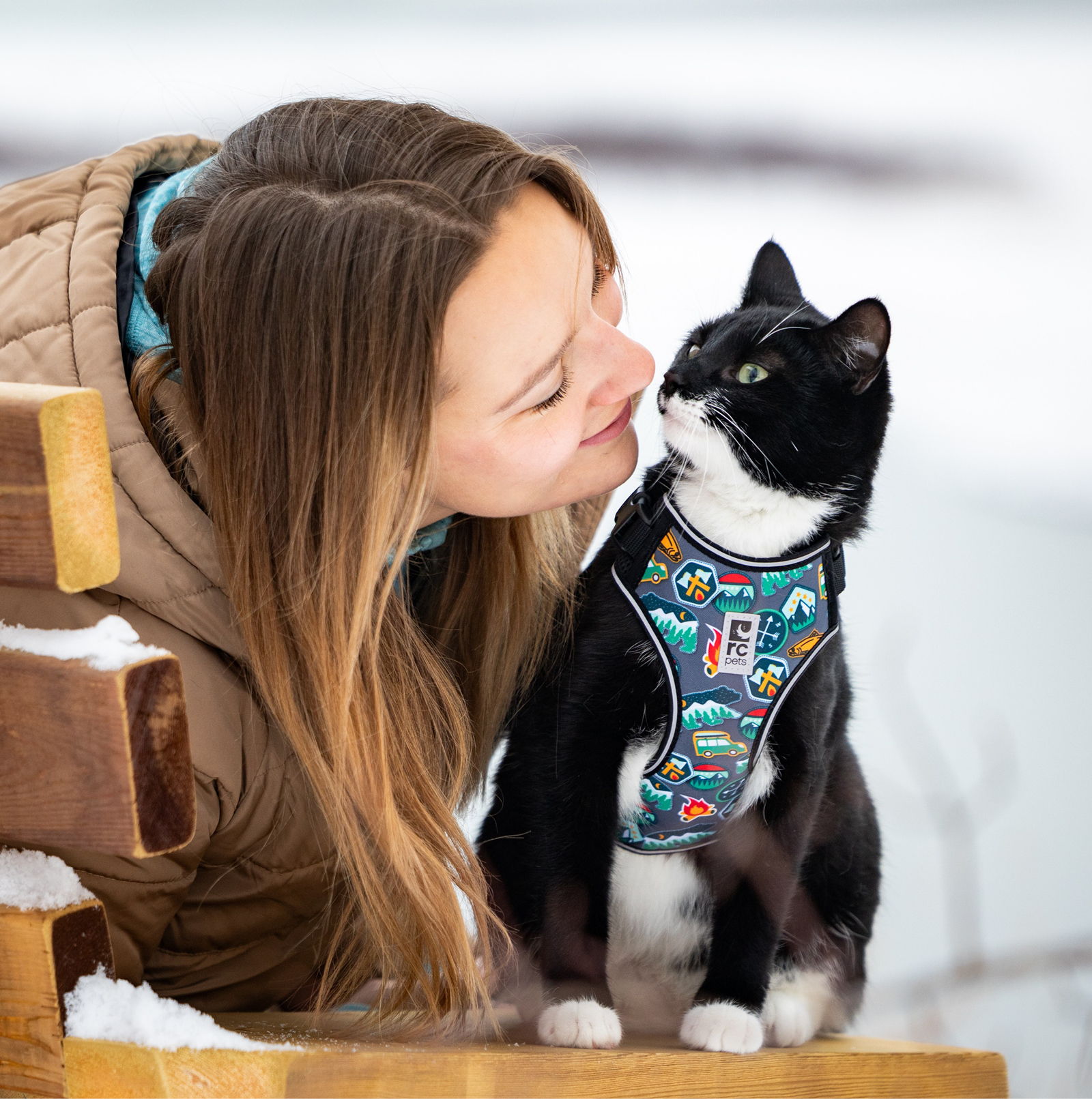 Woman and cat share a playful moment in a snowy outdoor setting.