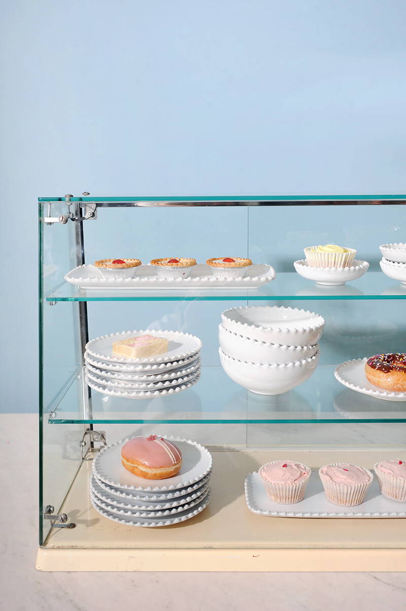 A vintage glass cake display case containing Pearl White china and  traditional tea time cakes.