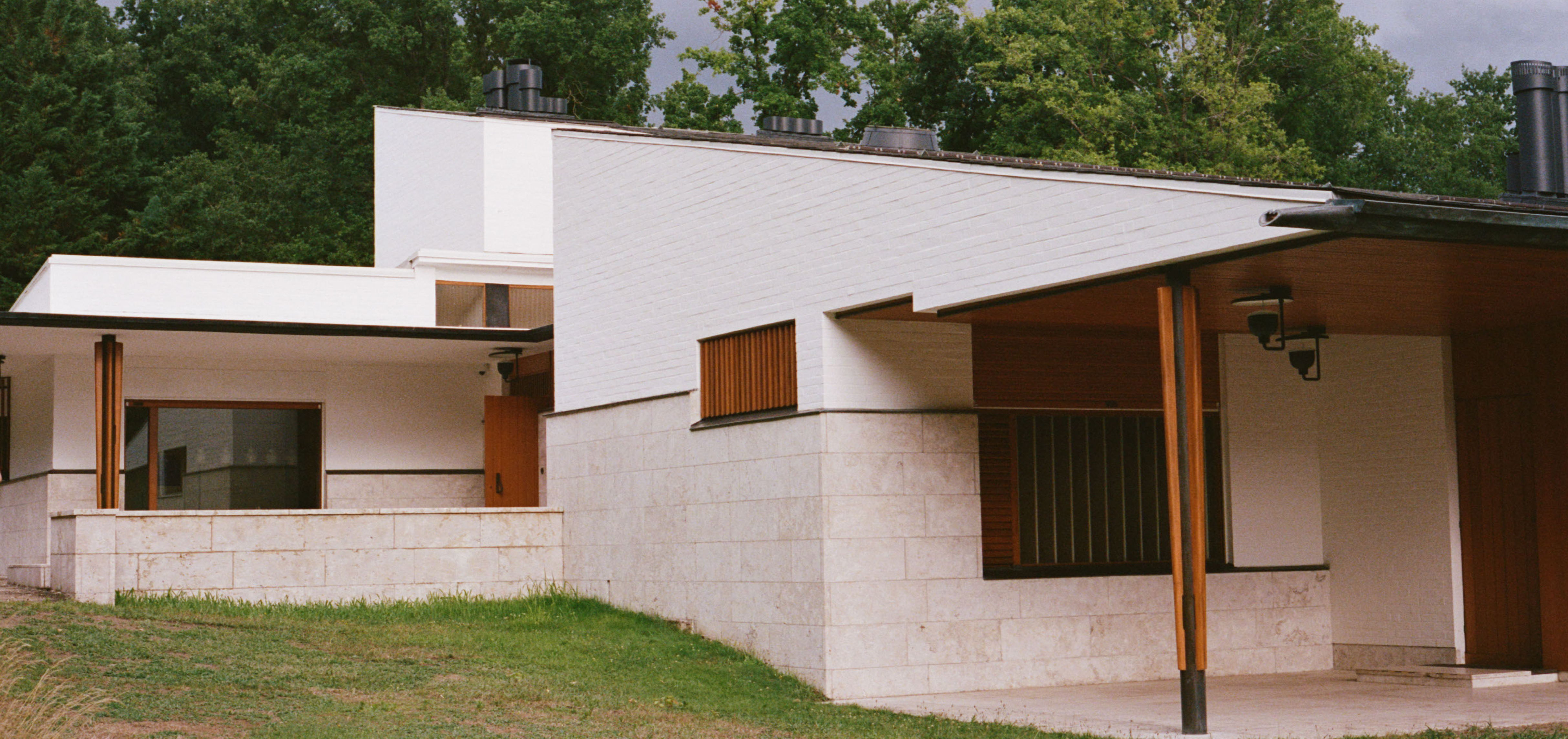Modern architectural house with white walls and wooden accents set in greenery.