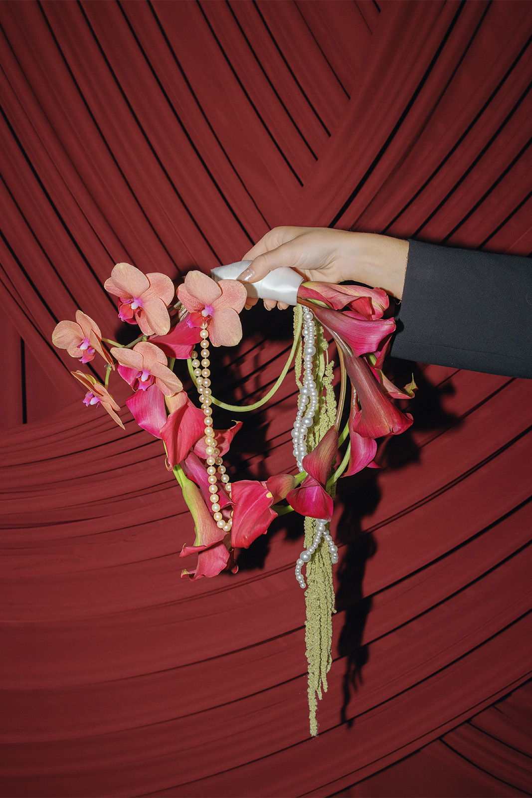 A hand holding a floral arrangement against a red backdrop.