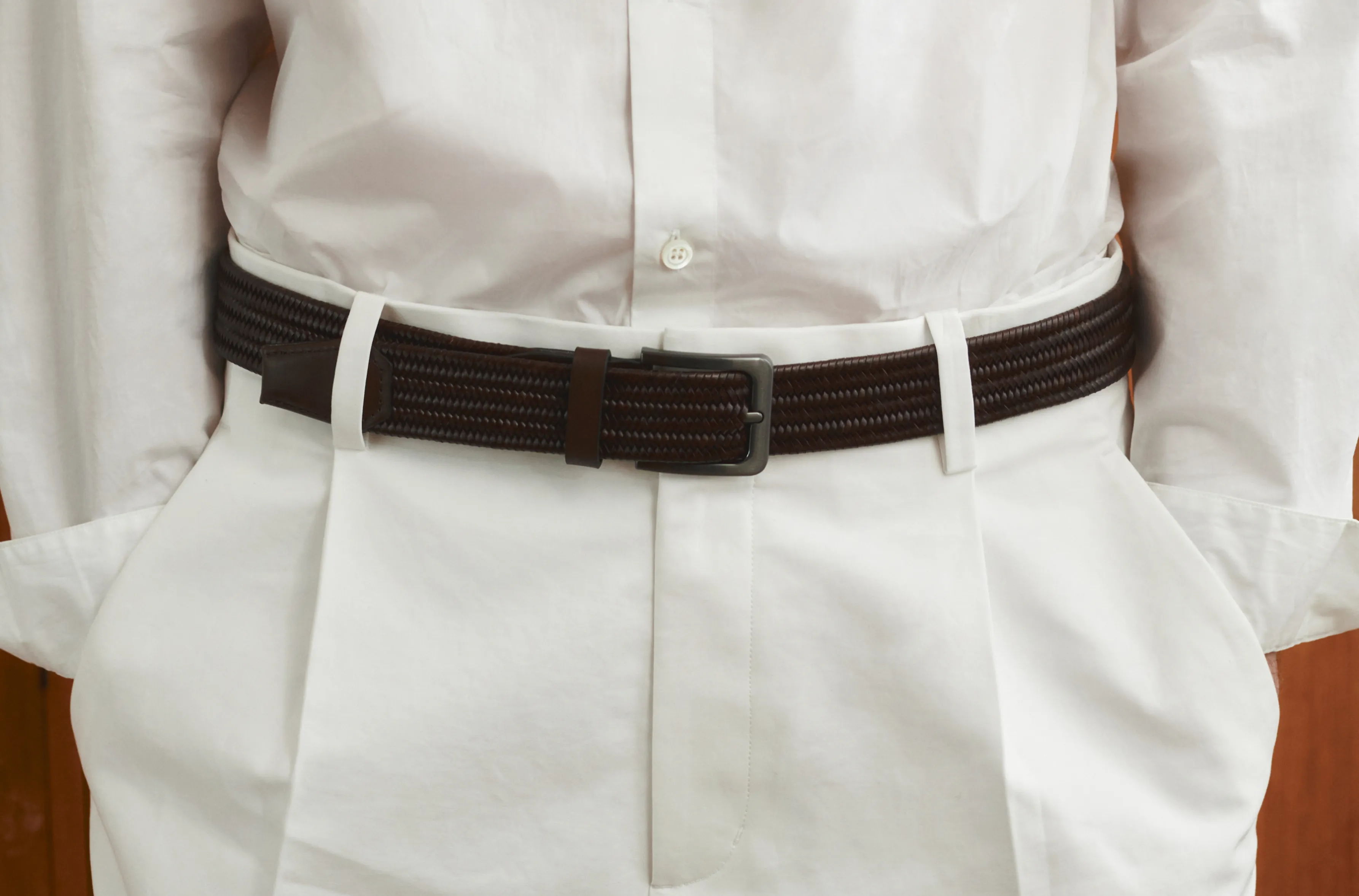 Person wearing a white shirt and brown belt, hands in pockets.