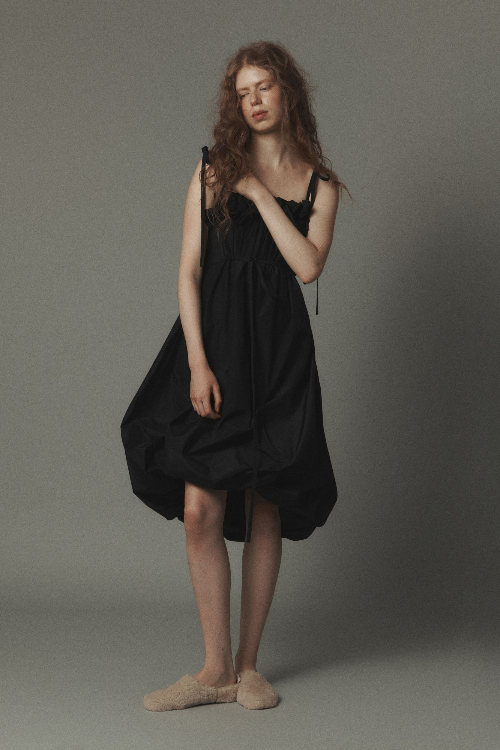 Model wearing a black dress, posing against a neutral background.