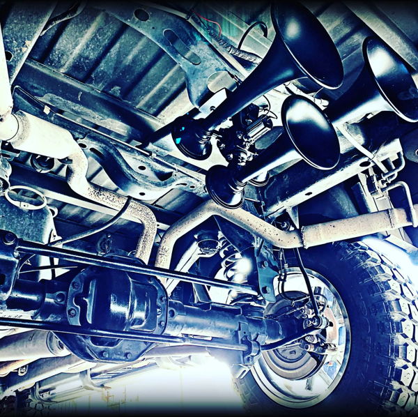Low-angle view of four-trumpet train horn kit mounted above rear axle on vehicle undercarriage