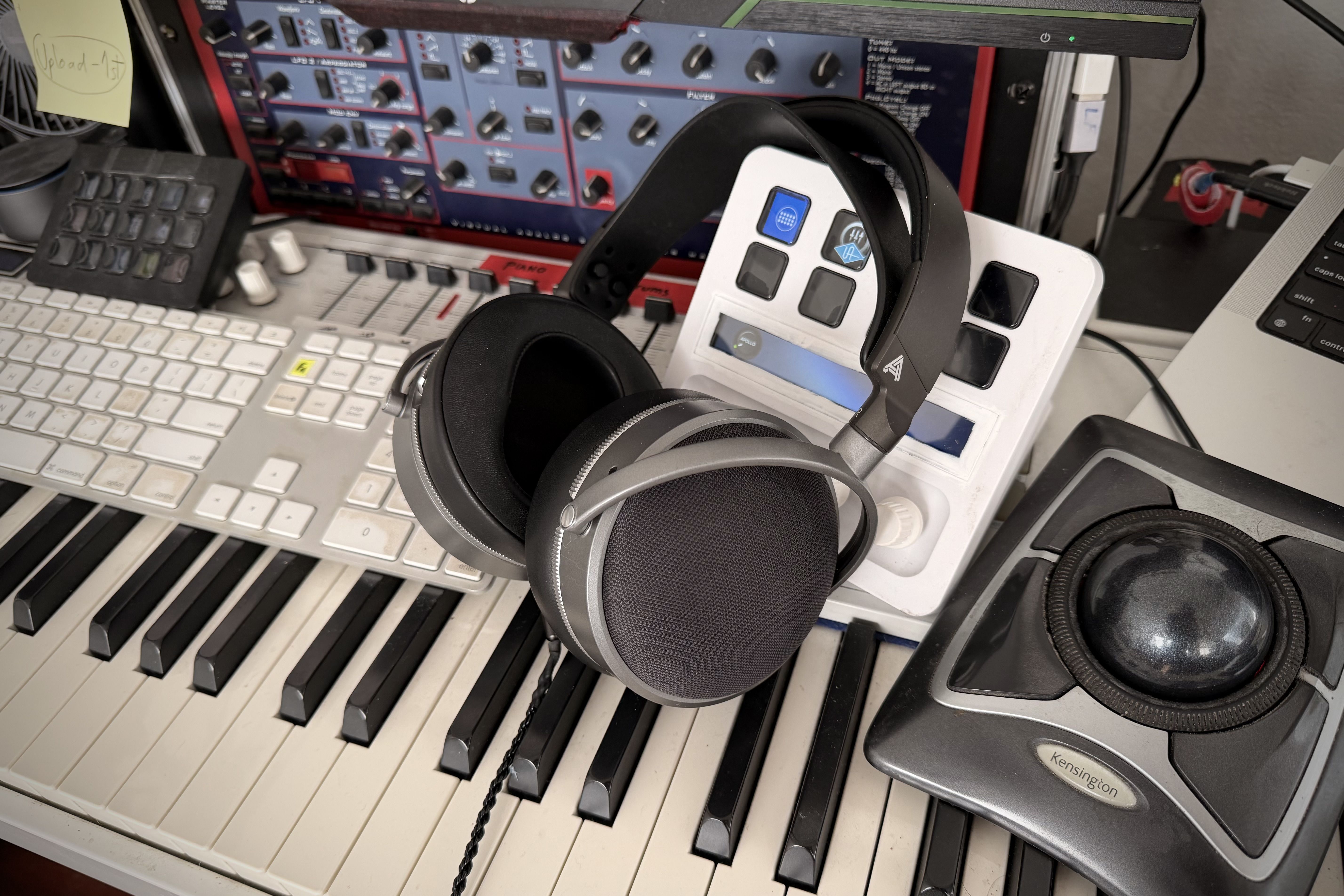 Audeze LCD-S20 headphones on a keyboard with music production equipment in the background.