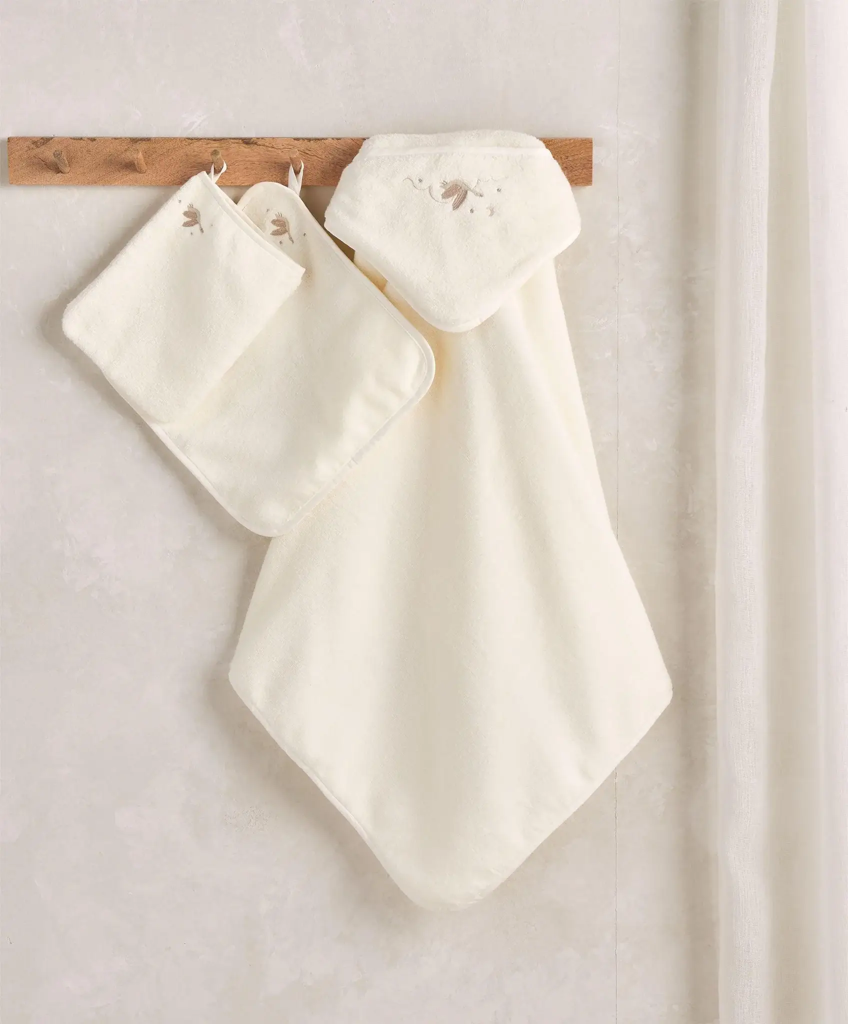 A cream-colored hooded towel and washcloth set hanging on a wooden hook.