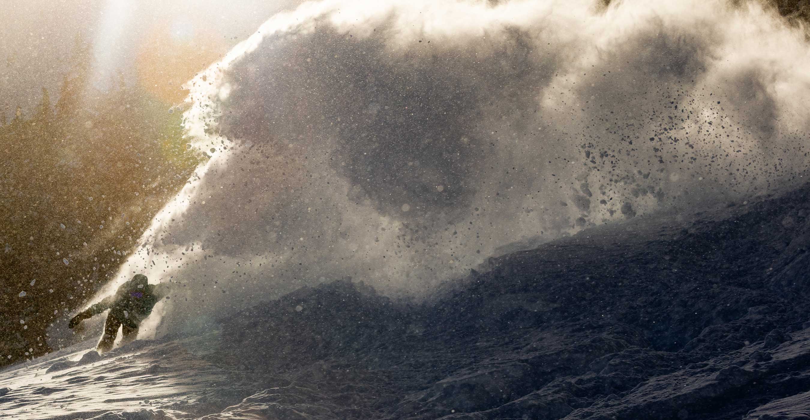 Snowboarder riding a wave with sunlight illuminating snow sprayed.