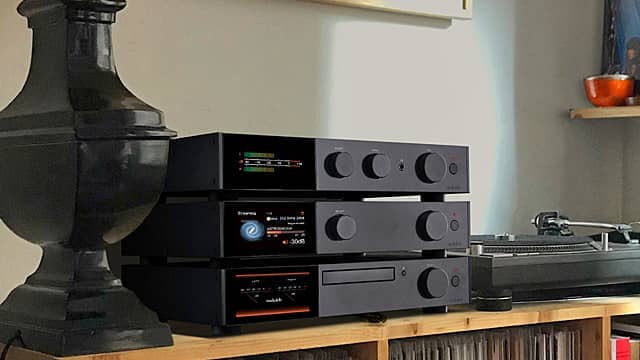 Audio equipment on a wooden shelf next to a lamp and turntable.