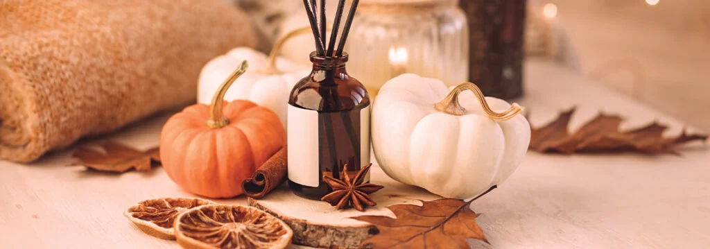 Decorative pumpkins, essential oil bottle, and autumn leaves on a table.