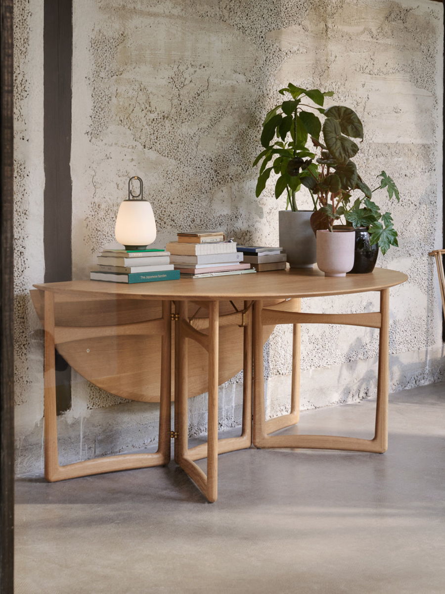 A wooden &Tradition HM6 Drop Leaf Extendable table with books and a plant in a modern setting.