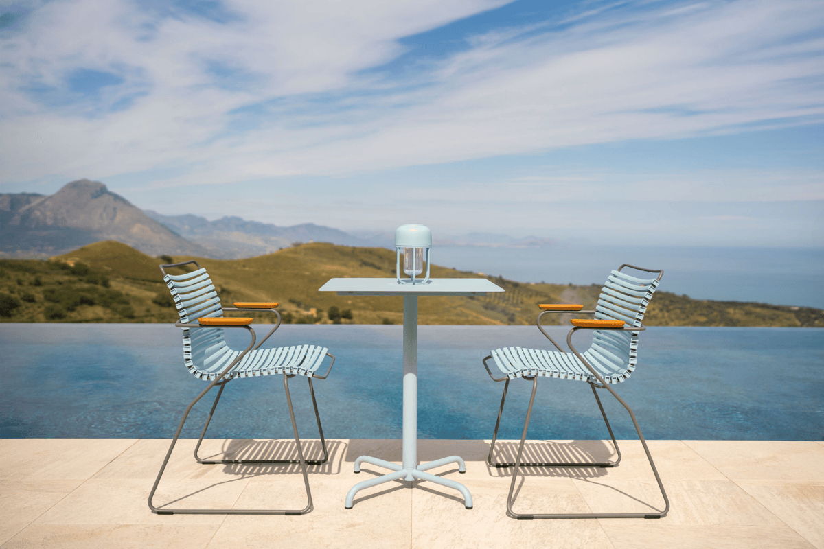 Two outdoor chairs facing each other across a small bistro table beside an infinity pool with a mountain and ocean view.