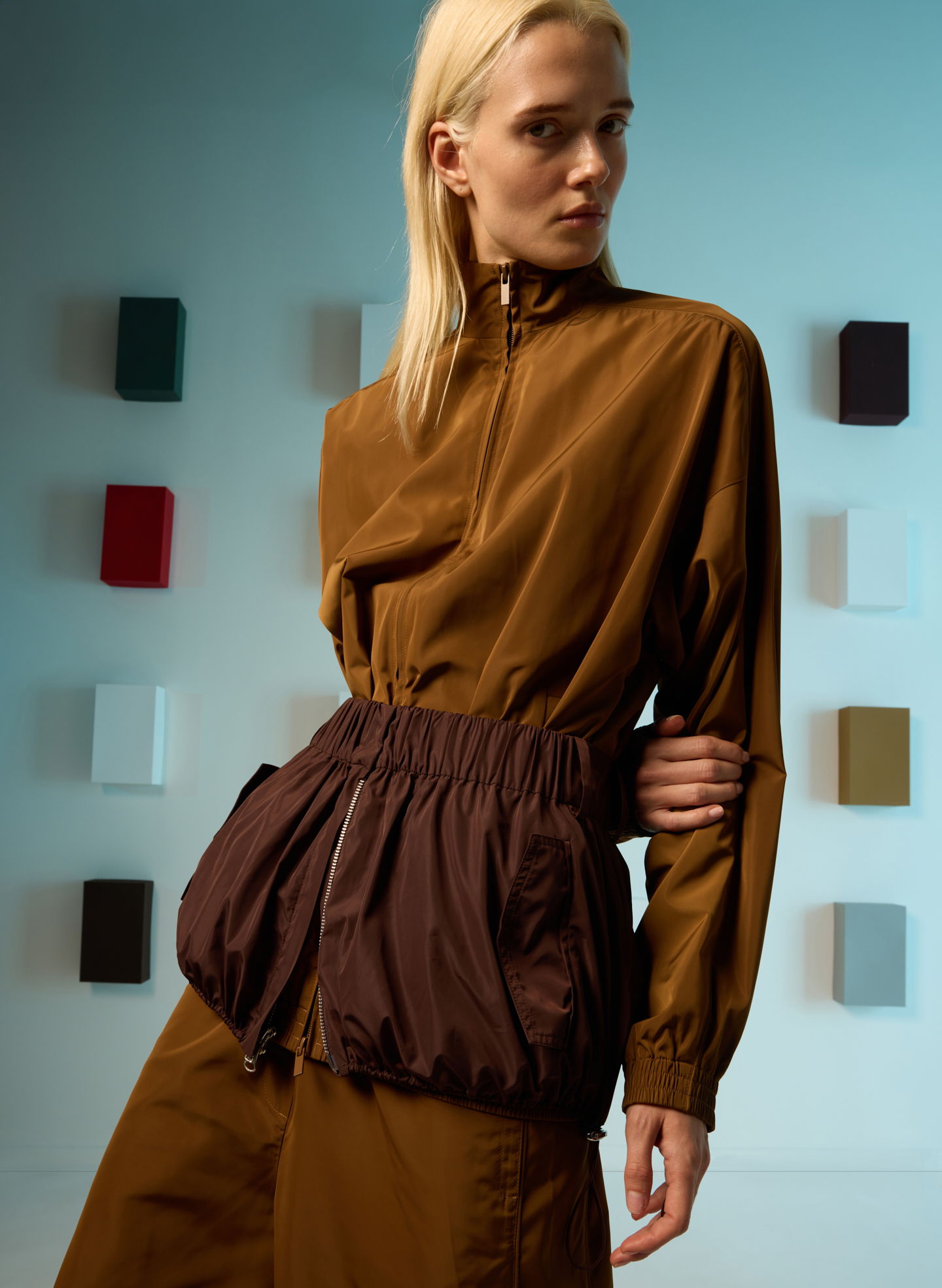 A model wearing a brown outfit with a cinched waist in a studio setting.
