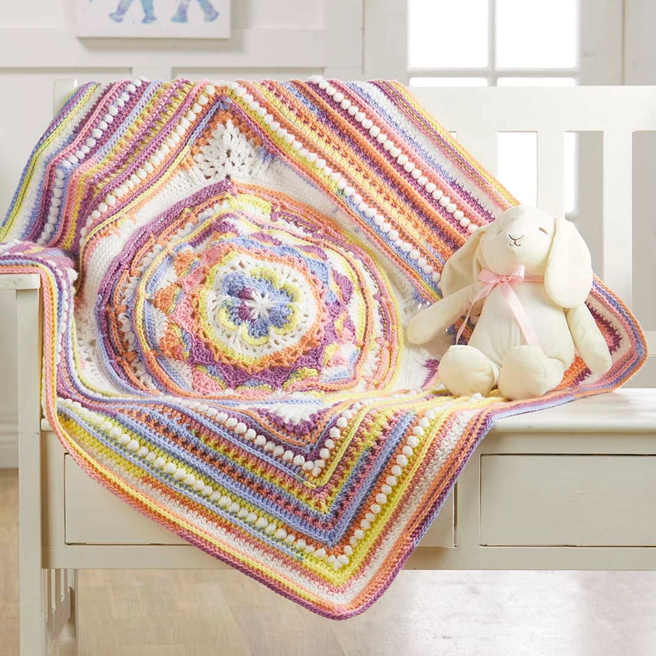 A colorful crochet blanket draped on a chair with a stuffed bunny.