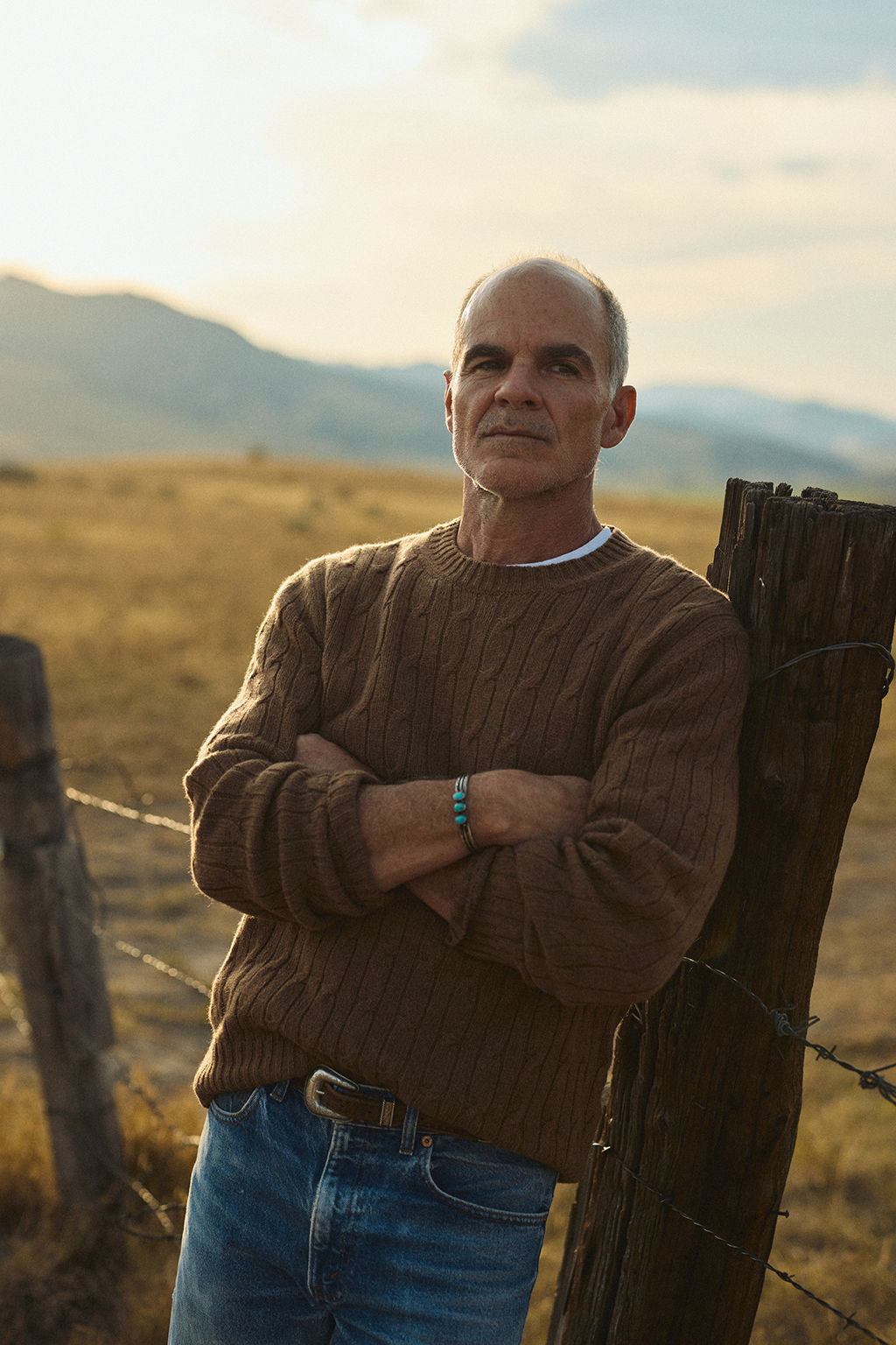 Michael Kelly leaning on a fence post wearing the Bowen Cashmere Cable Sweater in Saddle Brown in Pray, Montana