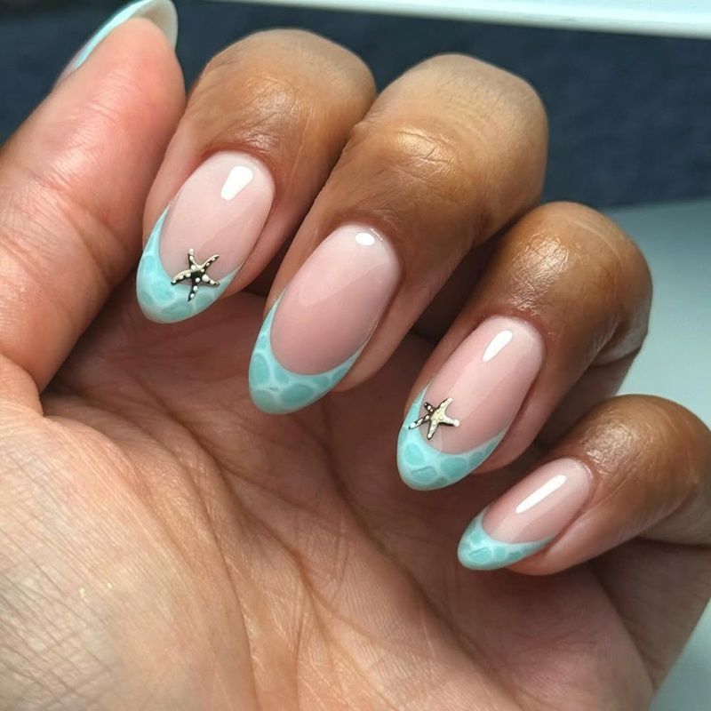 A hand with stylish pink and blue nail art with gold starfish accents.