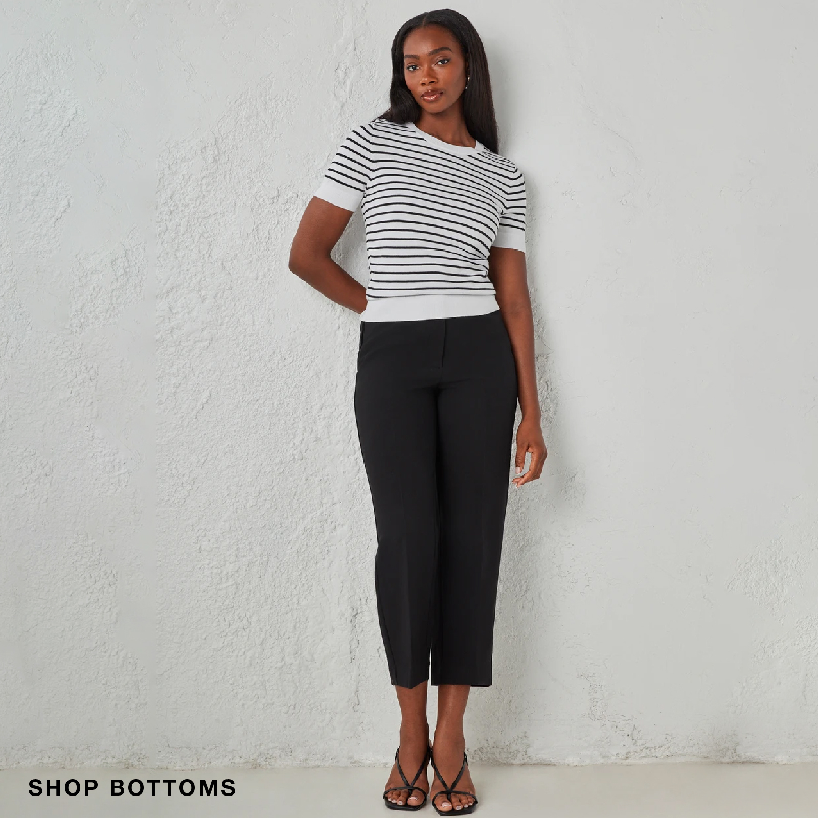 A woman in a striped top and black pants stands against a neutral background.