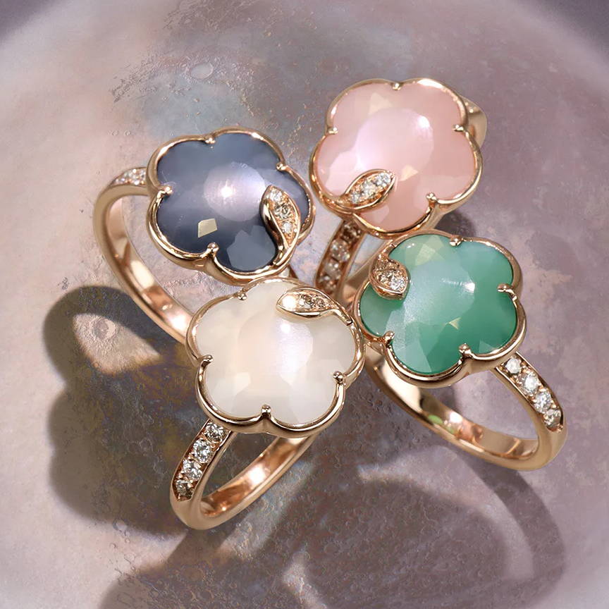 Four gold rings with colorful floral stones arranged on a circular background.