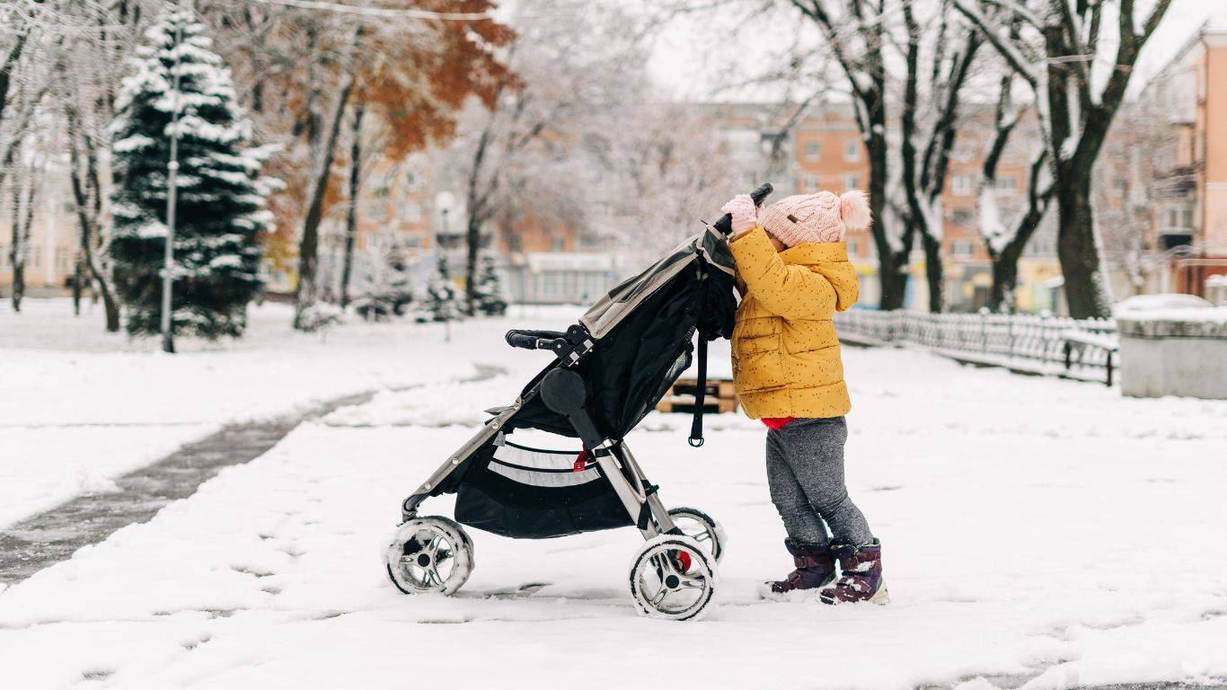 child pushing stroller through snow