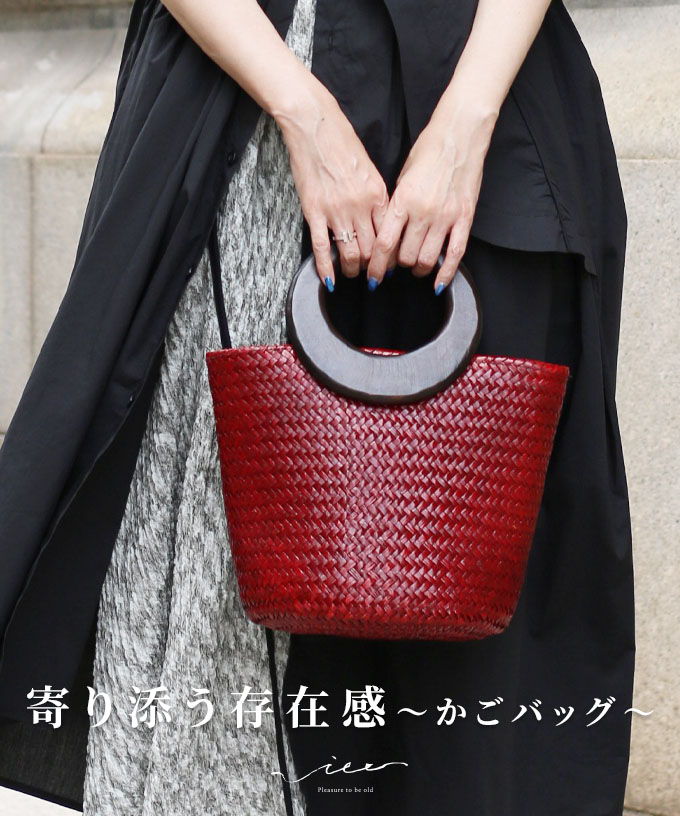 A person holding a red woven handbag, wearing a black outfit.