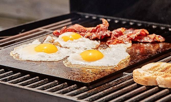 A Misen Oven Steel fries eggs and bacon on an outdoor grill.