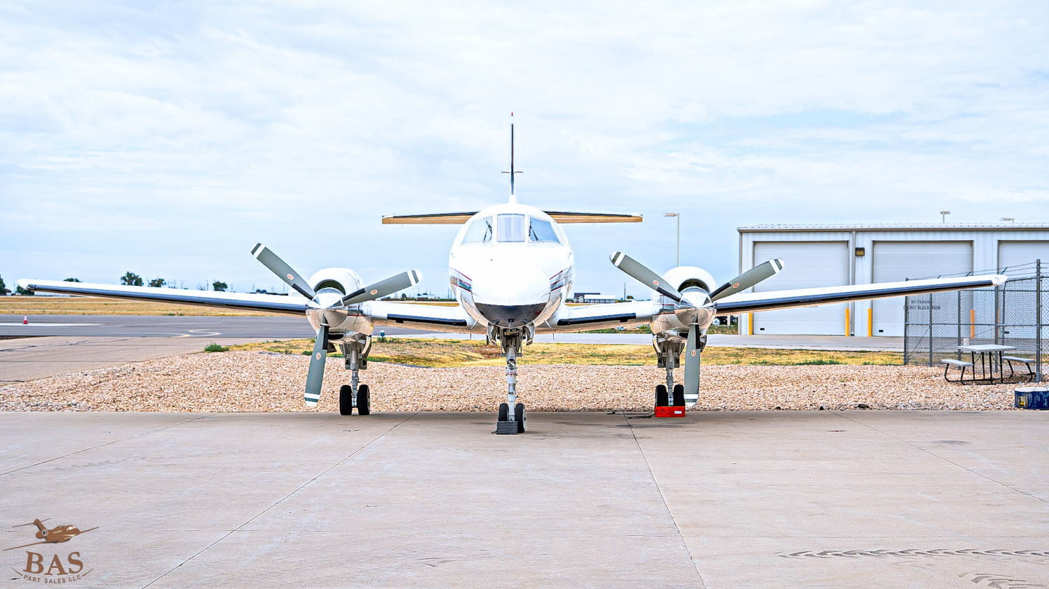 A small aircraft parked on a tarmac with hangars in the background.