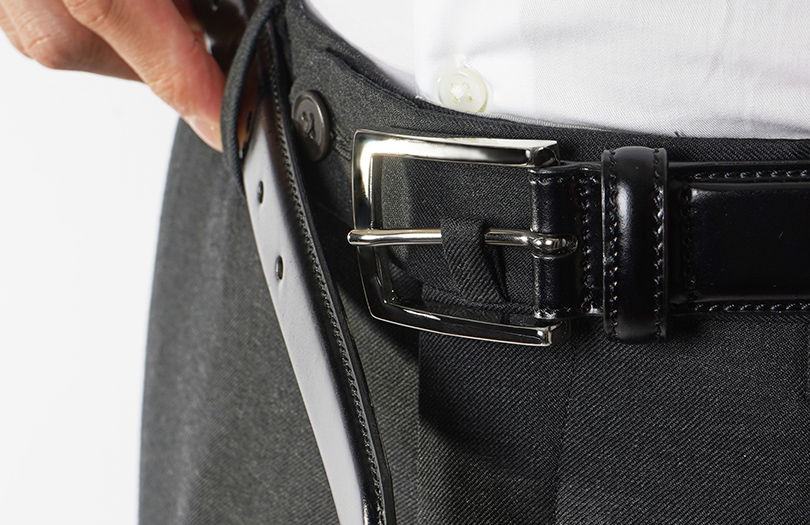 Person fastening a black belt on gray trousers.