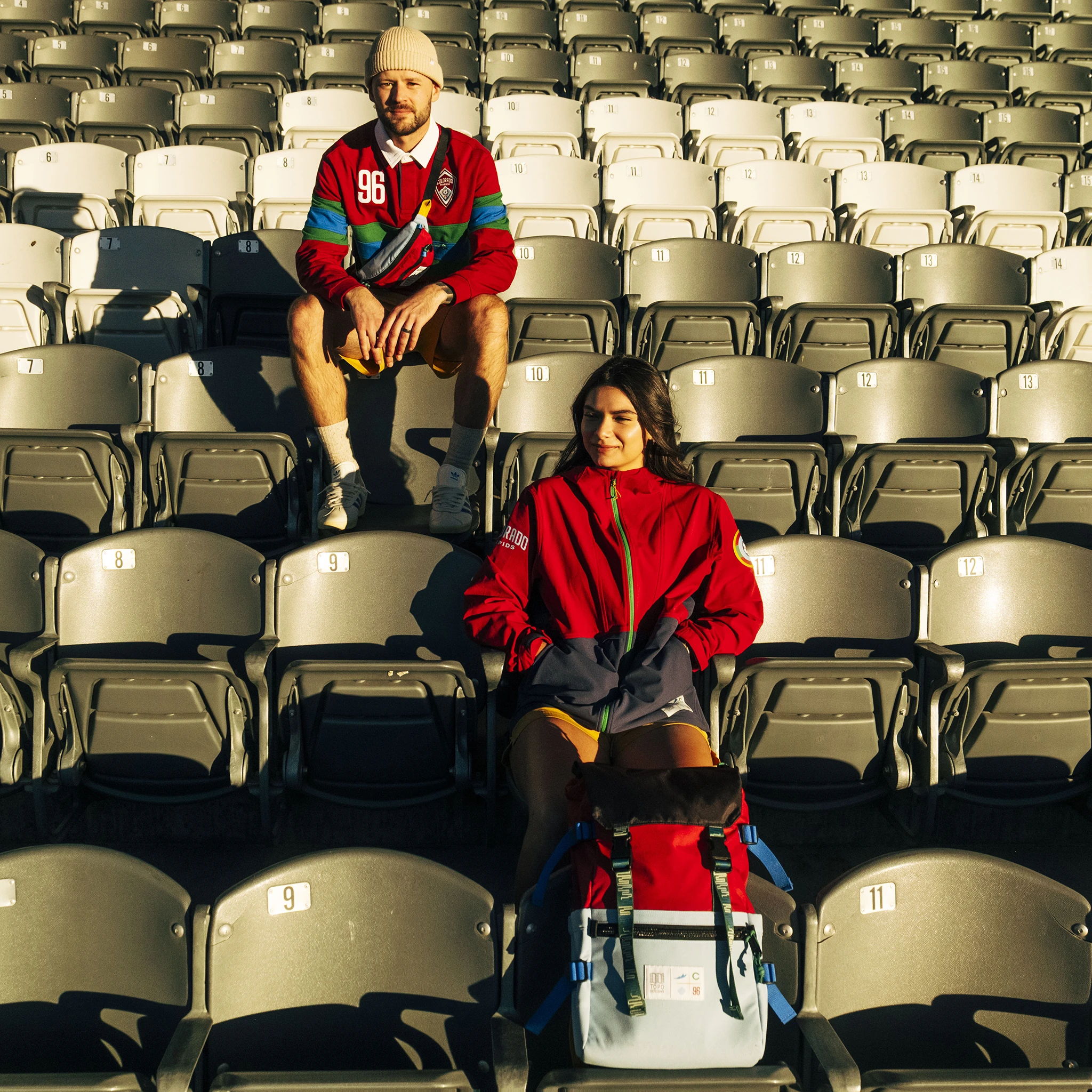 Two people sitting in empty stadium seats, one with a cooler.