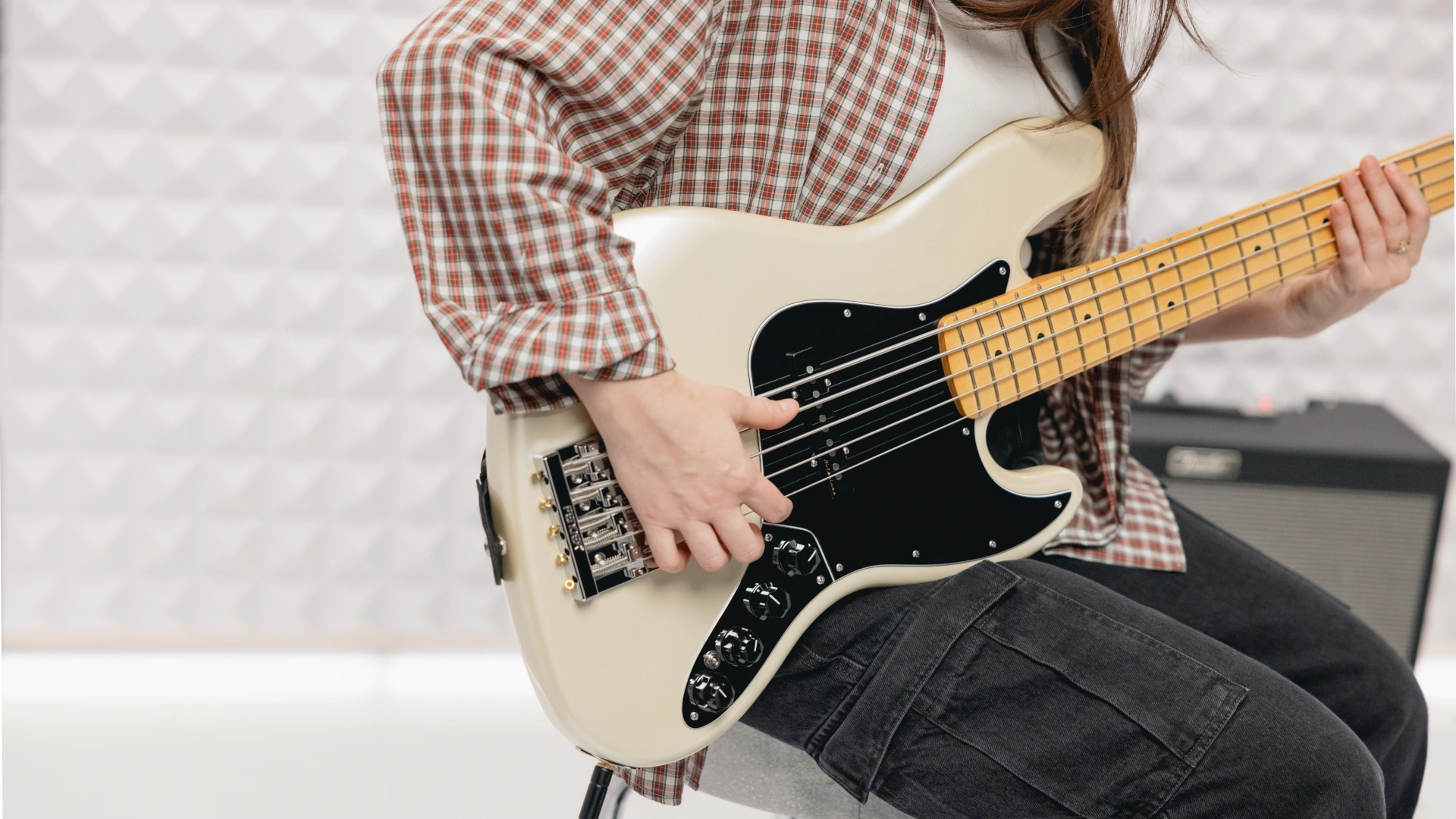 Person playing a cream Fender 5-string Jazz Bass guitar in a practice setting.