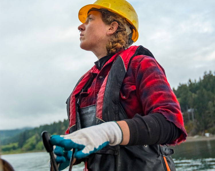 Woman in hardhat and flannel working on a boat.