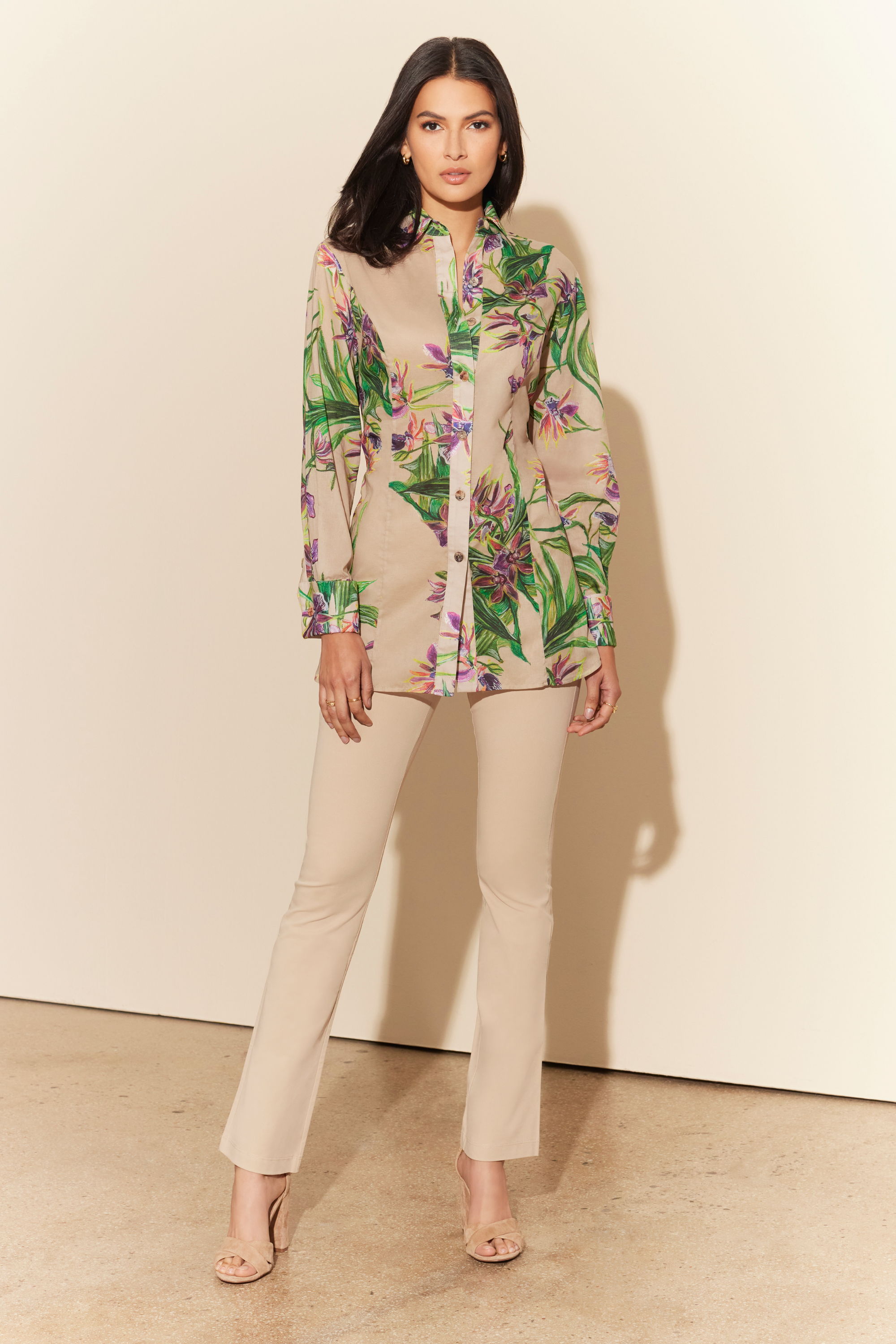 Woman in floral shirt and beige pants standing against a light background.