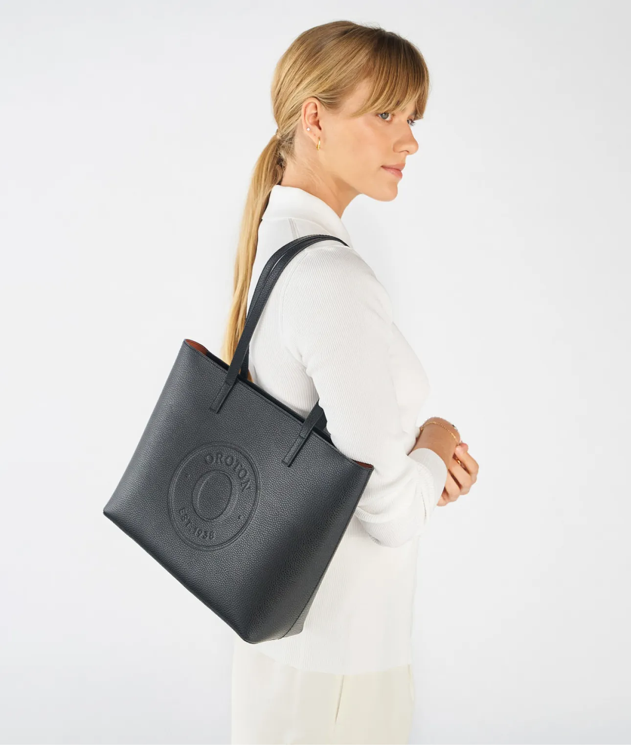 Woman in white top carrying a black tote bag.