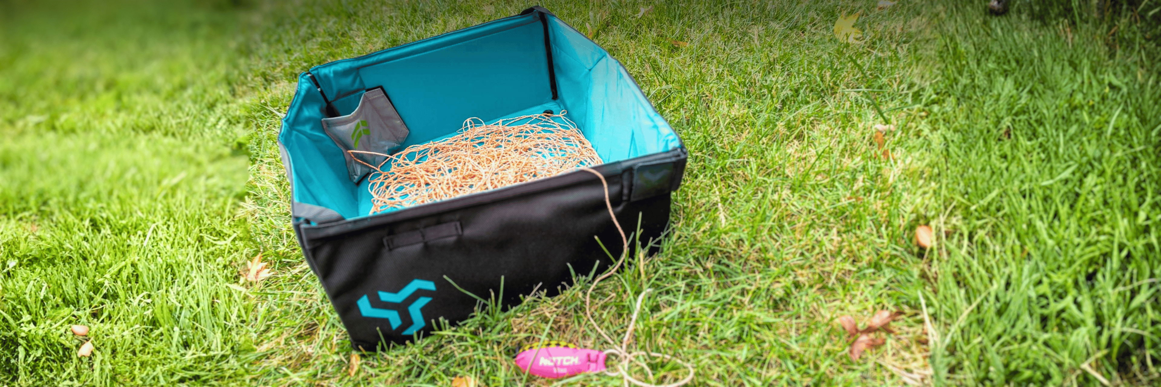 A blue and black container on grass, filled with sand or soil.