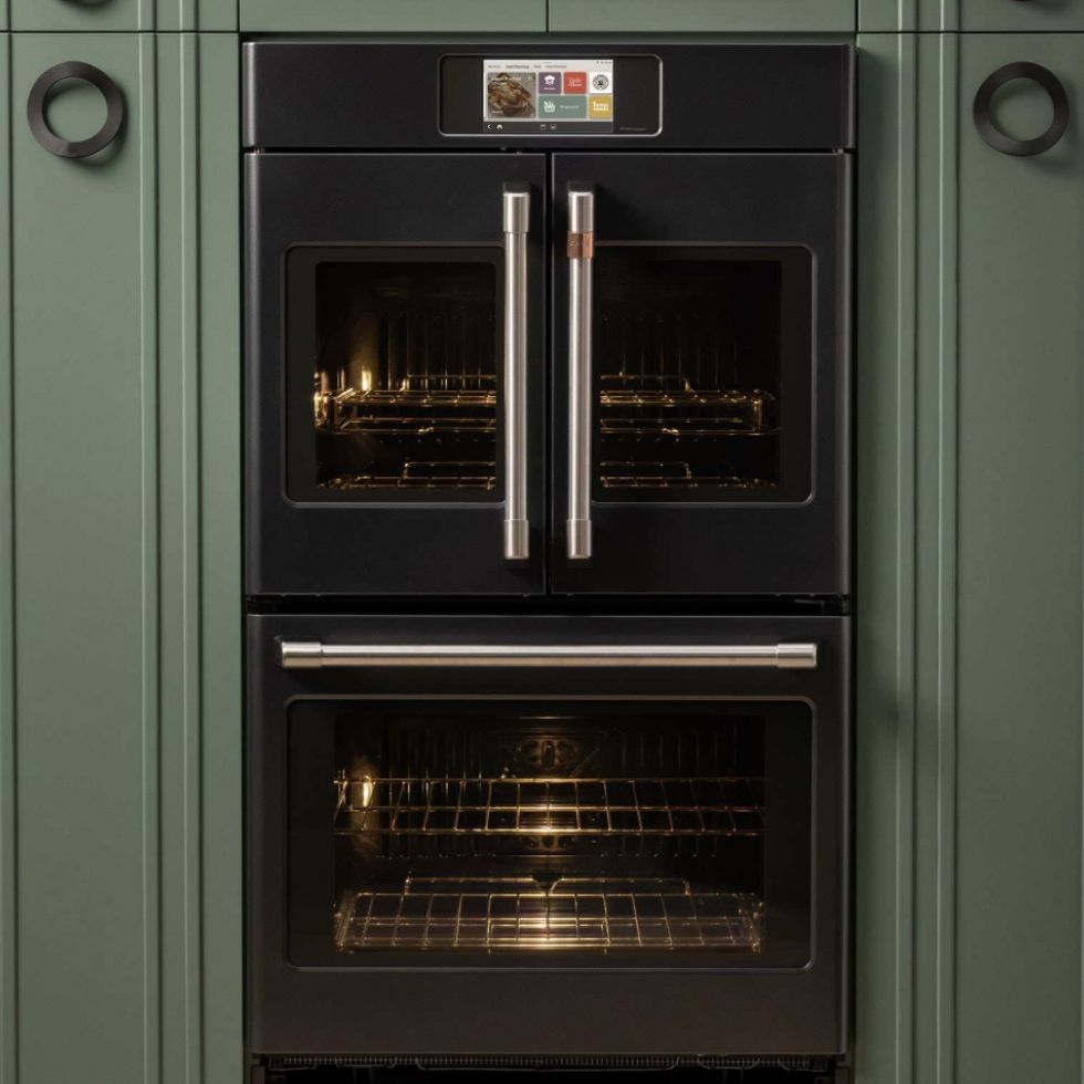 Black double oven built into a green kitchen cabinet.