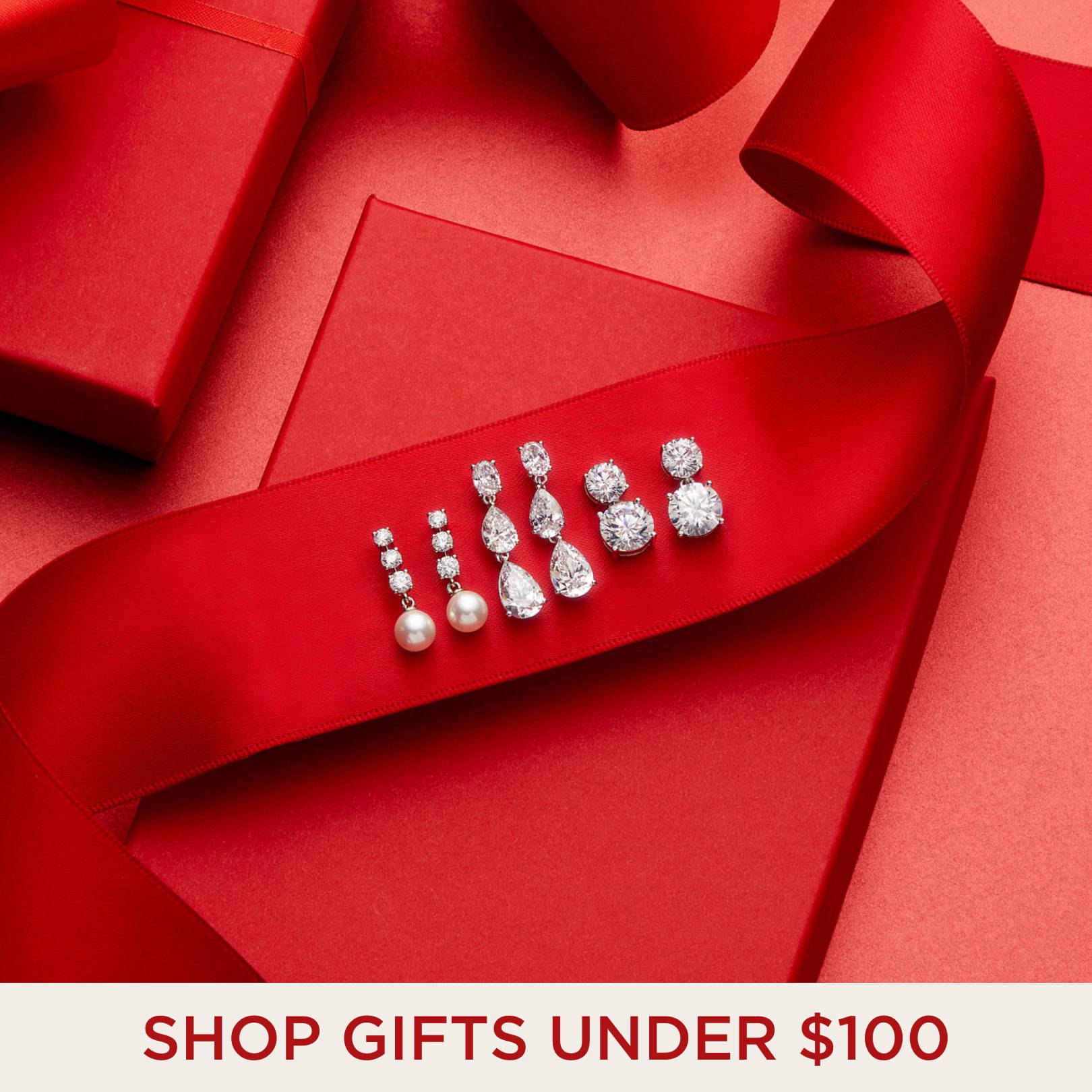 SHOP GIFTS UNDER $100. Image of three pairs of cubic zirconia drop earrings on top of a red ribbon. 