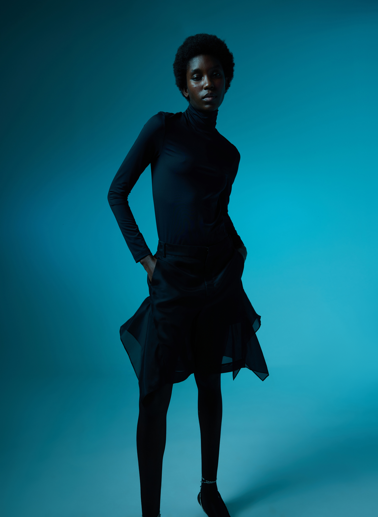 A model in a black outfit poses against a blue background.