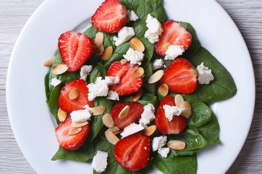 spinach salad on a white plate with slice strawberries, slivered almonds, and goat cheese