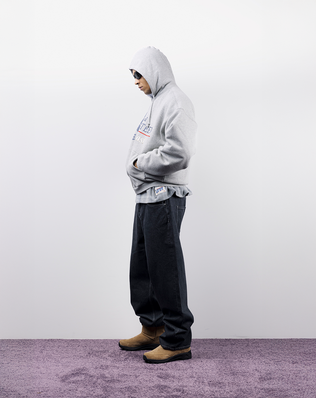 Person in a gray hoodie and dark pants standing on purple carpet.
