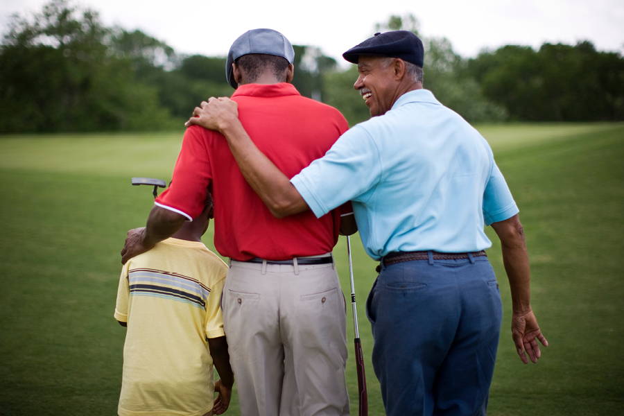 3 generations of men on golf greens smiling with arms around each other