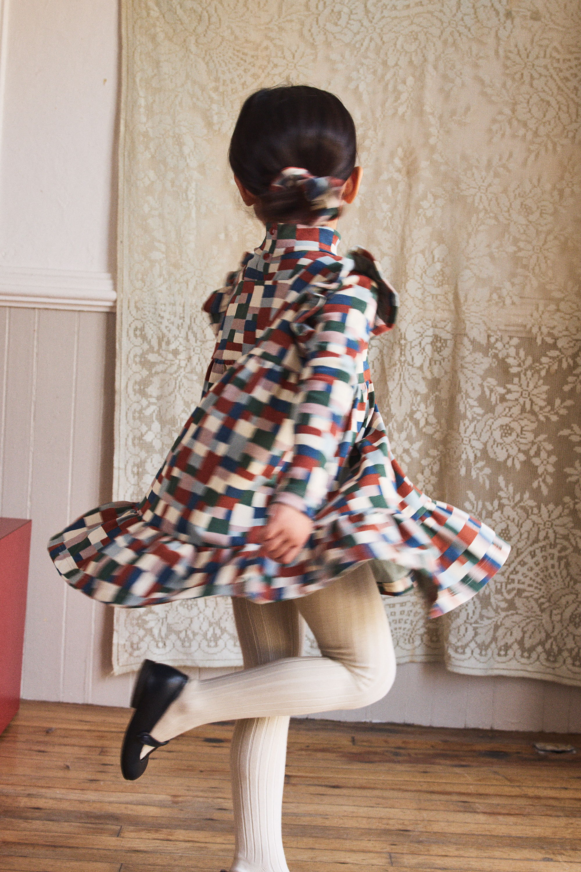 Child twirling in a colorful dress against a patterned background.