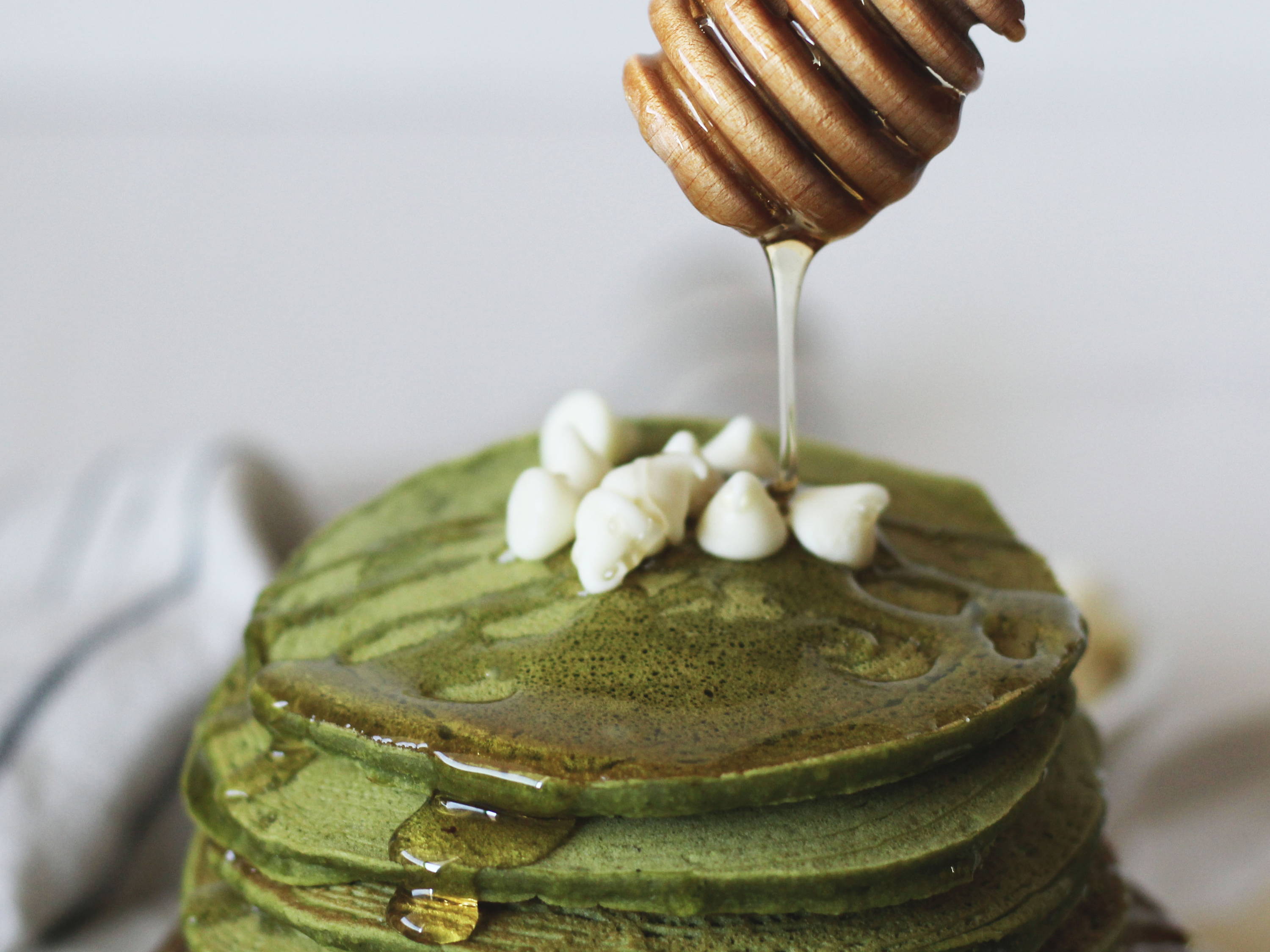 Honey drizzling over green pancakes topped with small dollops of cream.