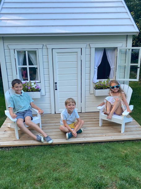 Kids sitting on the wooden playhouse terrace by WholeWoodPlayhouses
